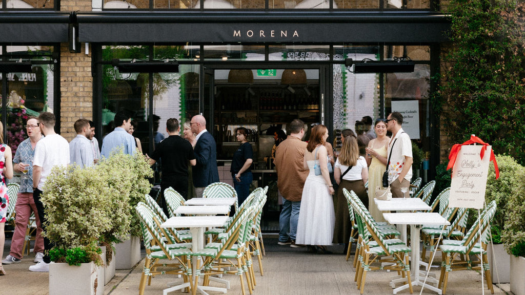 People gathered outside a restaurant named 'Morena' with outdoor seating.